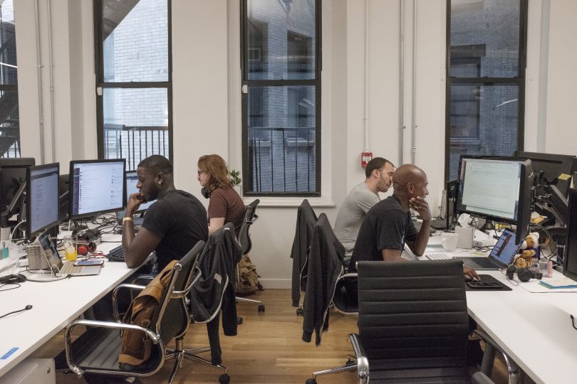 NS1 employees working at bench-style desk seating in the office