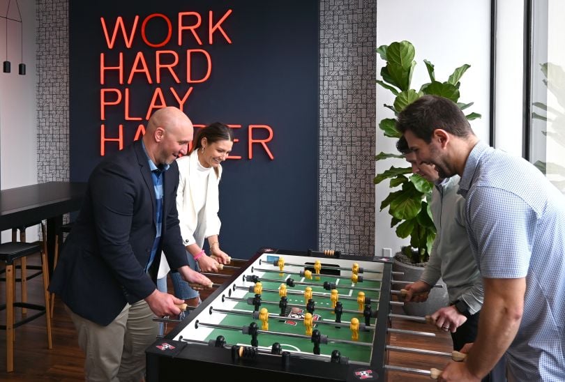 Photo of Center team members playing foosball with "Work Hard Play Hard" sign on wall behind them