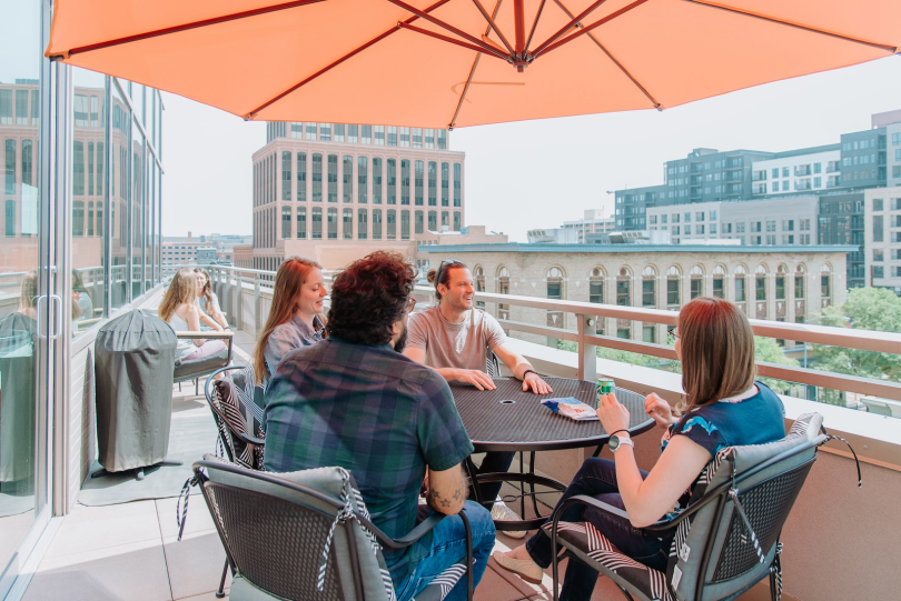 Pie Insurance's Denver office outdoor patio with employees sitting around a table under an orange umbrella. The city skyline is visible in the background.