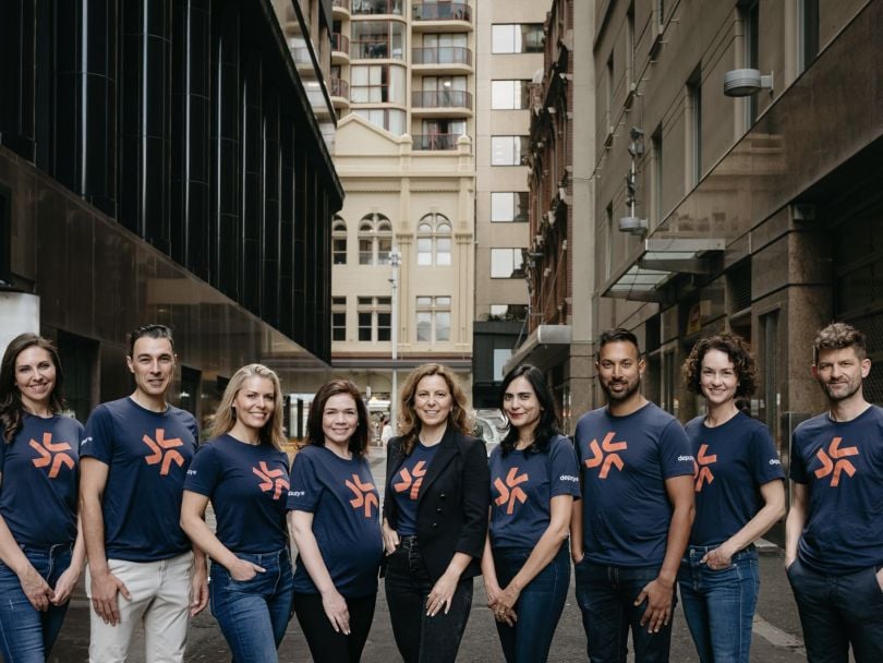 Deputy employees pose in matching company t-shirts on the streets outside their office.