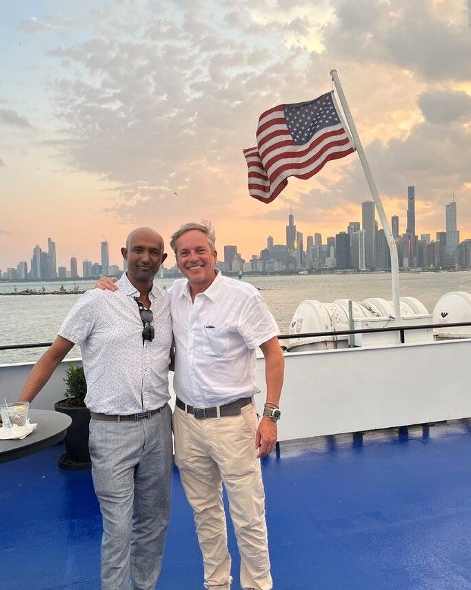 Two teammates stand on a boat in front of a sunset. Caption: Soaking in the stunning Chicago skyline during our office dinner cruise, a perfect blend of leadership and inspiration. (Geneva Trading)