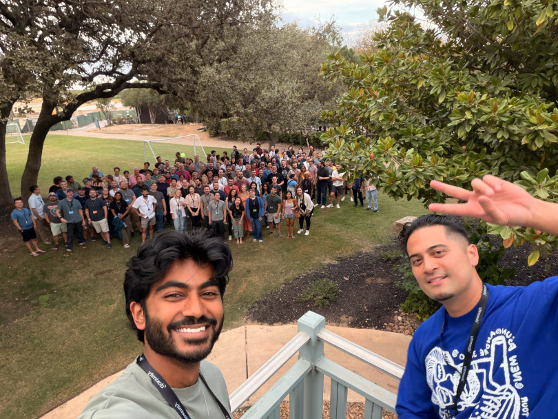 Two Doximity team members pose for a selfie while a large group of their peers pose in the background