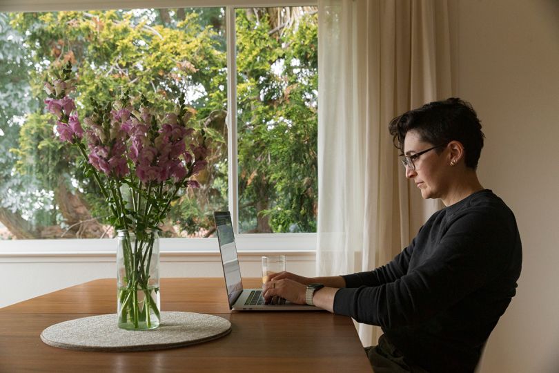 Rachel Wolan working from home at a table with a vase of flowers on it