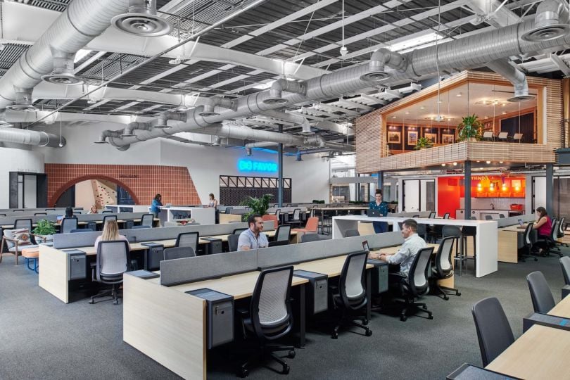 Employees chat at an open-concept work space reminiscent of a library. A board room is seen on the second level. It looks like a tree house.