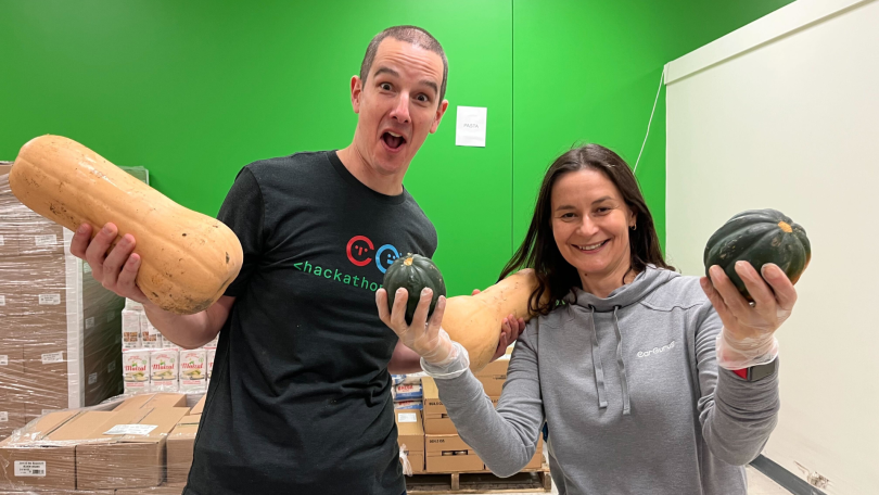 Two CarGurus team members hold gourds at a food drive.