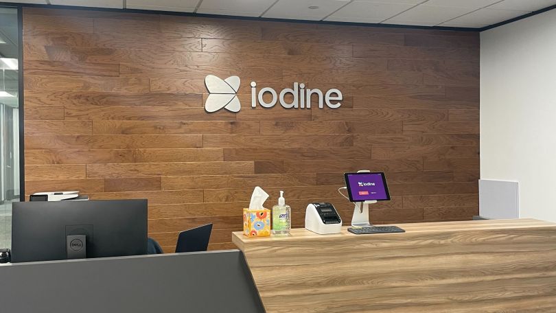 Iodine’s reception desk area, in front of a wood paneled wall featuring its logo.