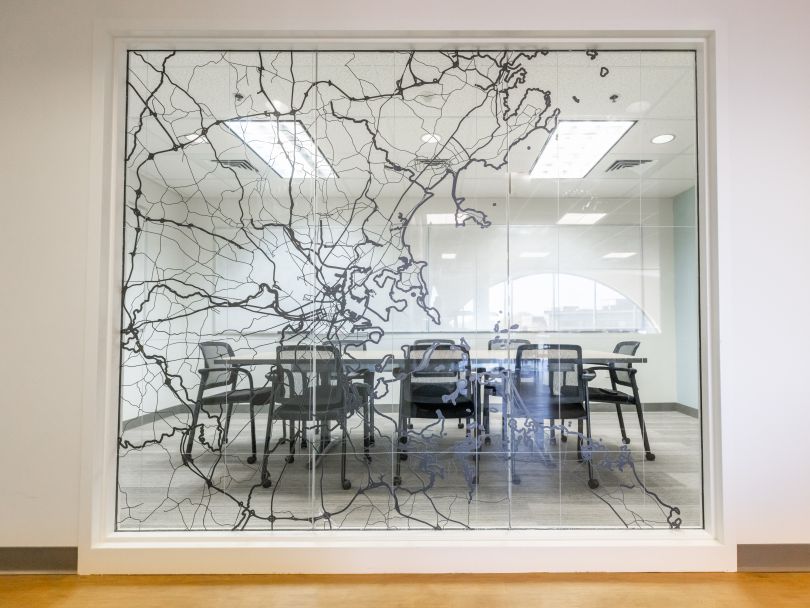 A glass conference room door shows a map of the greater Boston area