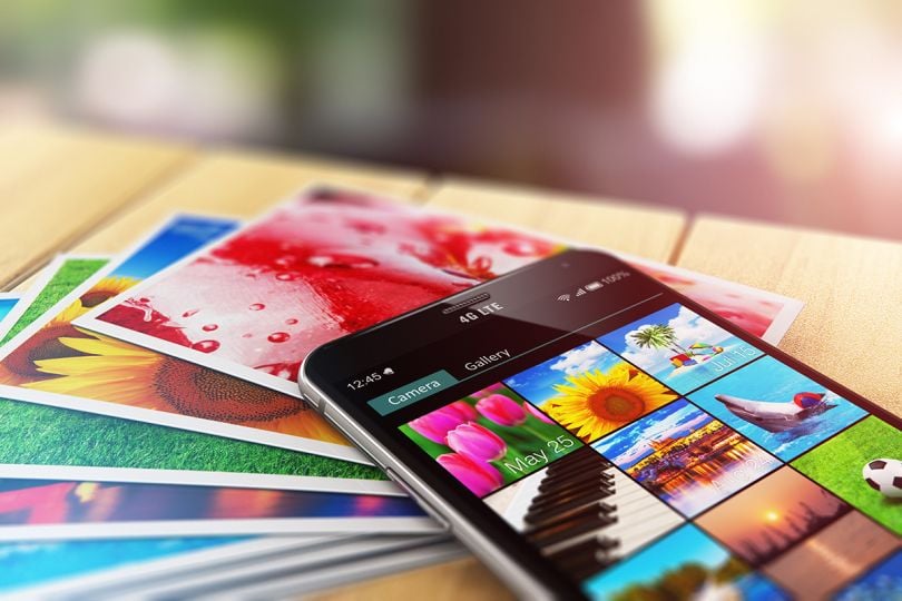 view of stack of color photo pictures and smartphone with image gallery app on the screen