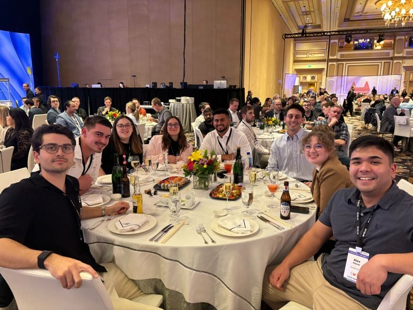 GitLab Account Executive Eddy Popat poses for a photo alongside several colleagues seated at a table during the company’s annual sales kickoff in Las Vegas