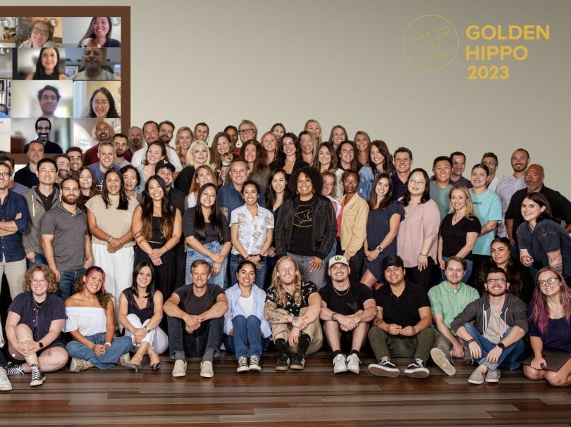 The Golden Hippo team poses for a large group photo that includes a Zoom grid of remote employees in the background.