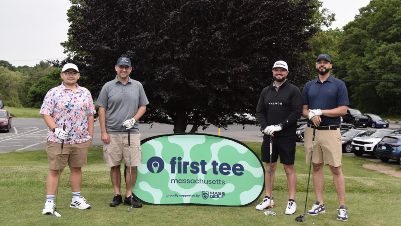 Four CarGurus team members holding golf clubs stand at a golf event near a banner that reads “First Tee Massachusetts.”