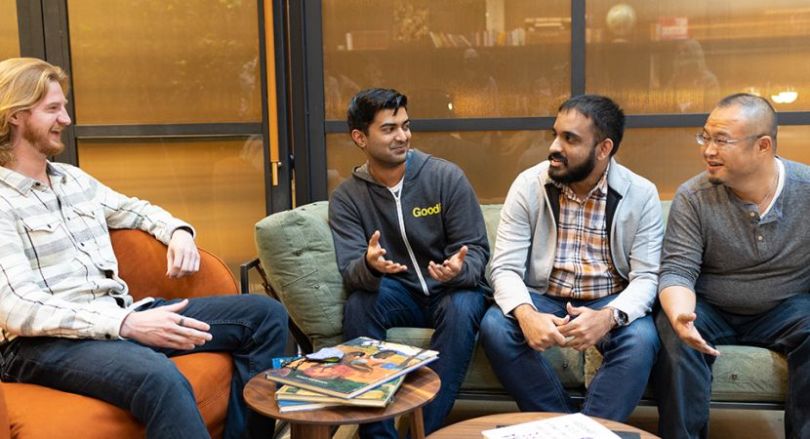  GoodRx team members sit in office lounge area together, talking and smiling.