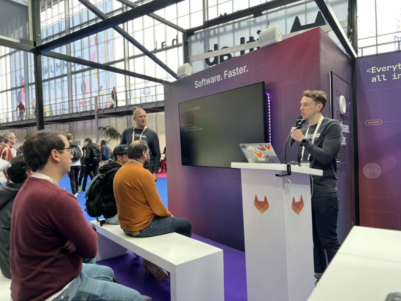 GitLab booth with presenter at podium talking to audience of people