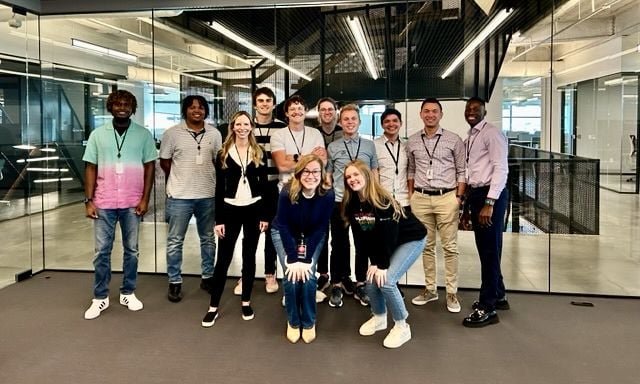 Pluralsight team members pose for group photo near glass wall in office.