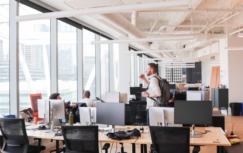 Photo of Kalderos office space, with an employee standing and talking to a seated coworker.