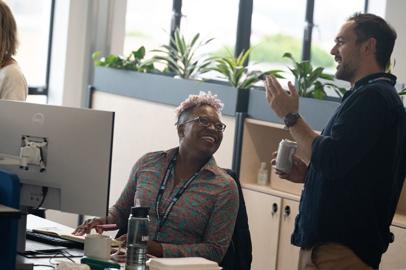 Immersive Labs team members smiling and laughing while having a conversation in the office