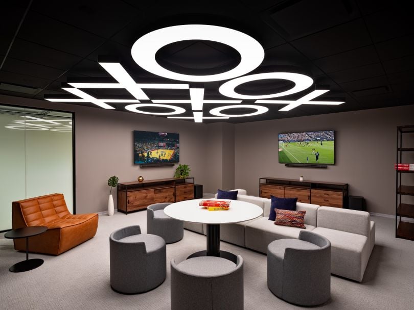 A game room in one of Justworks’ office locations, equipped with two wall-mounted TVs, a couch, several chairs and a table