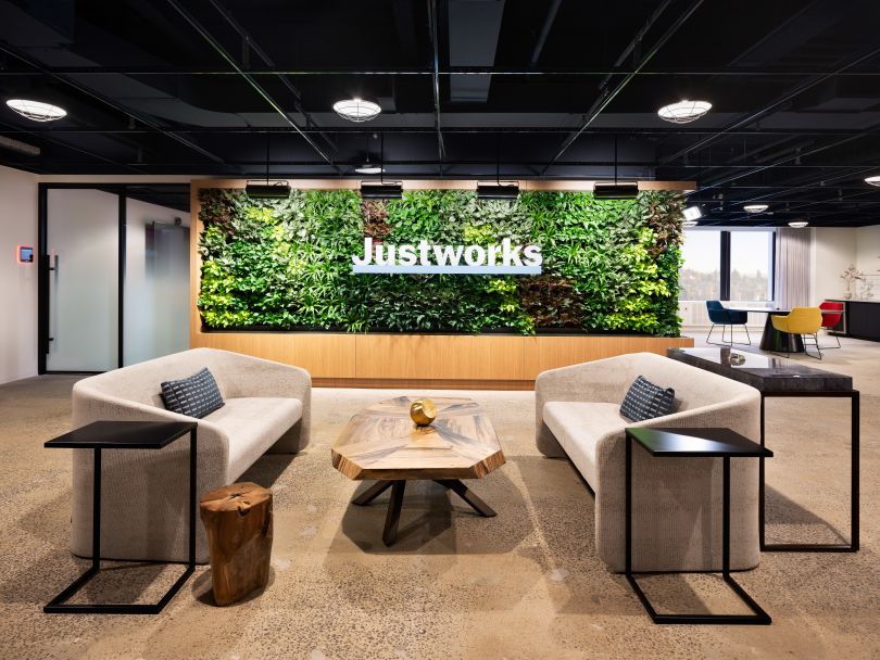 A lounge space in a Justworks office location in which the company’s logo is printed on a wall behind two couches and a table
