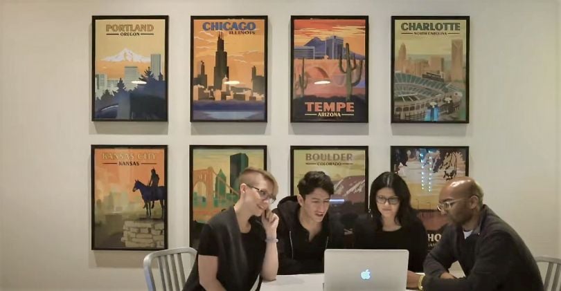 Four KUBRA team members looking at a computer with a wall of city posters citing KUBRA’s U.S. offices on the wall behind them. 