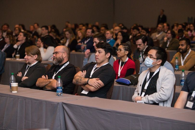  A group of Level Access employees sit and listen to a speaker in a large lecture hall 