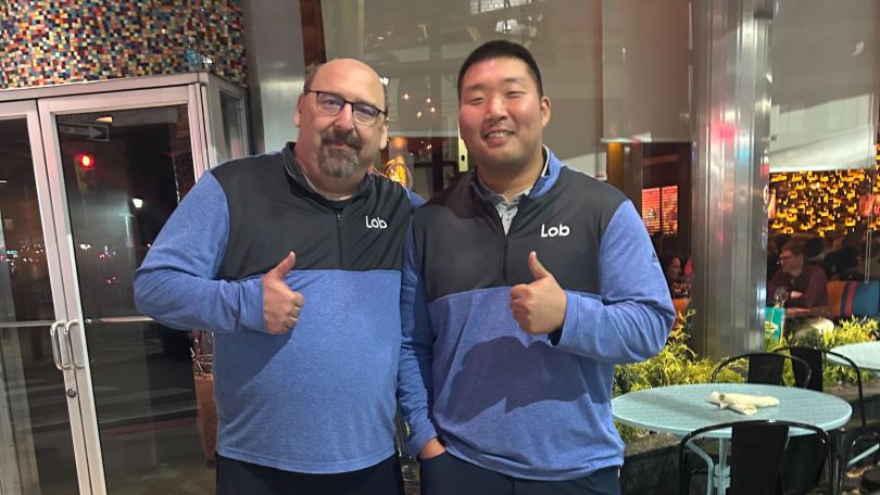 two Lob teammates wearing matching Lob fleece jackets give thumbs up signs and smile