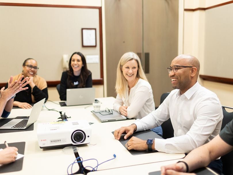 Telesign team members sit together at a conference table during the company’s recent Revenue Kickoff event, talking and smiling.