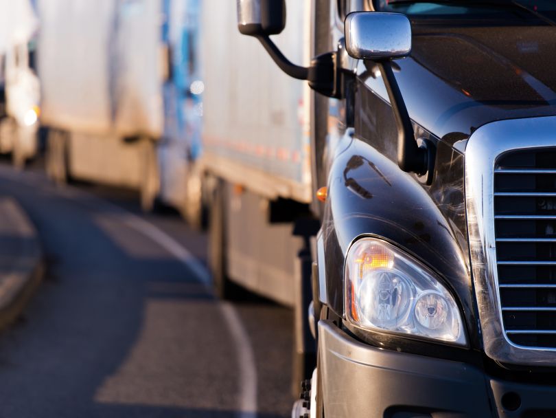 A photo of four semi-trucks lined up on a curving road.