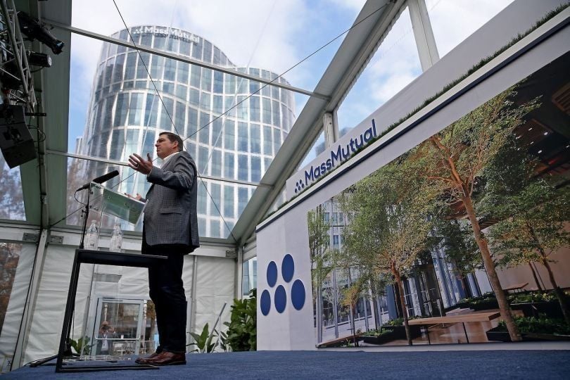 A man in a suit standing in front of a MassMutual building. He is standing in front of a microphone and giving a speech.