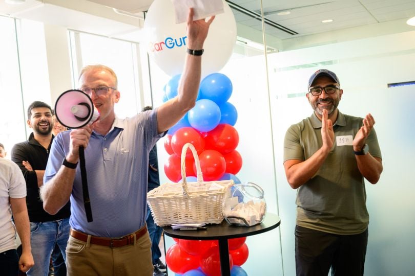  Ismail Elshareef clapping as a coworker speaks through a megaphone in front of a crowd during an office celebration.