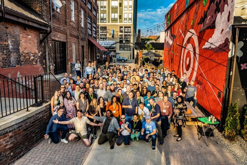 A group of employees from May Mobility stand outside between two buildings on a sunny day