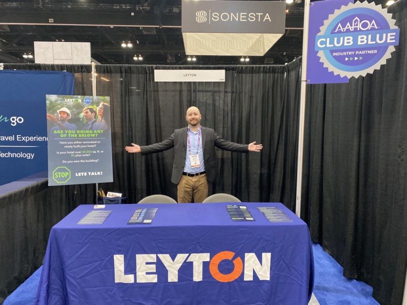 Man stands at Leyton booth at an expo, arms out to show off the setup.