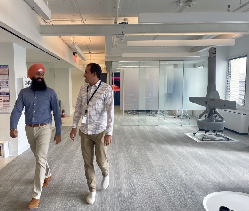 Two Shield AI employees walk down a hallway near a model of a drone. 