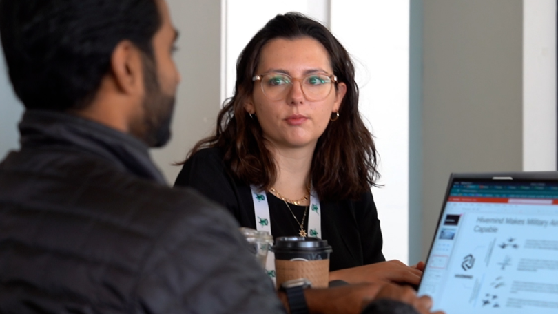 Two Shield AI employees chat over a computer and coffee. 