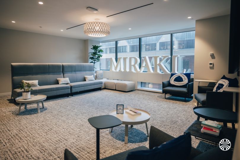 A lounge space in Mirakl’s office featuring a couch, several tables and chairs and the company’s logo displayed against a window