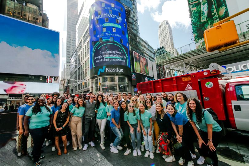 A large group of Multiverse employees poses beneath a Multiverse billboard in Times Square