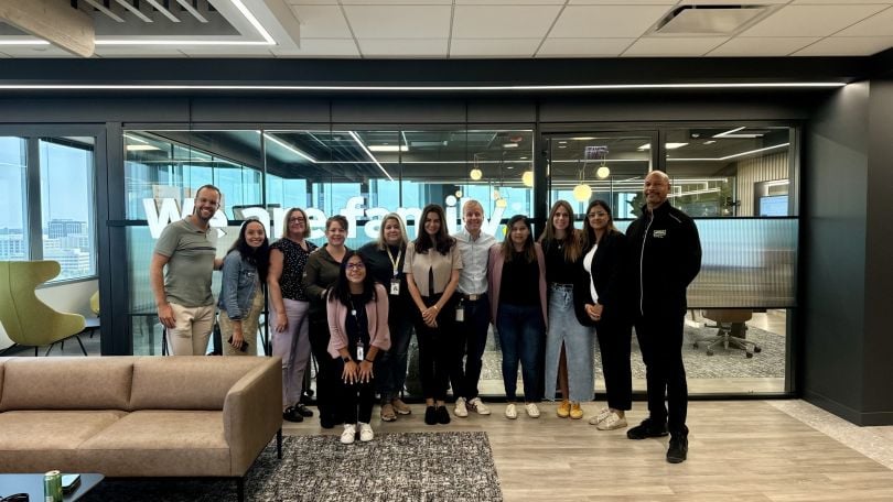 McCain Foods’ North American DEI Council members stand in an open modern office in front of a glass wall that reads “we are family.”