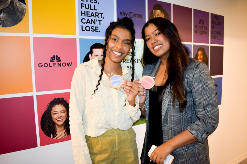 two nbcu colleagues pose for a photo in front of a wall