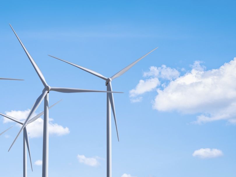 A photo of several wind turbines with a blue sky and clouds behind them.