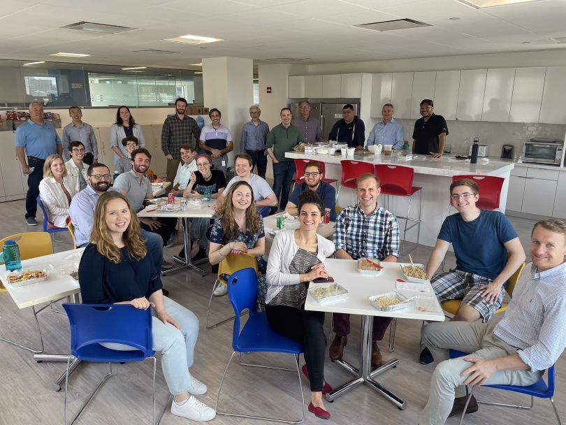 OM1 employees smile at the camera while sitting around tables in an office with food