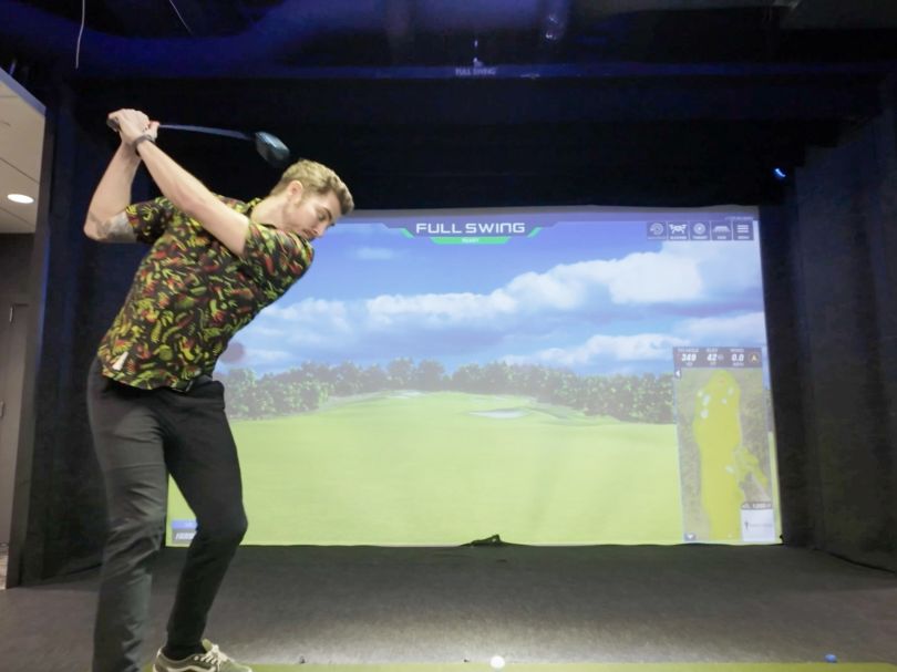 An Own Company employee swings a golf club in the office’s golf simulator.