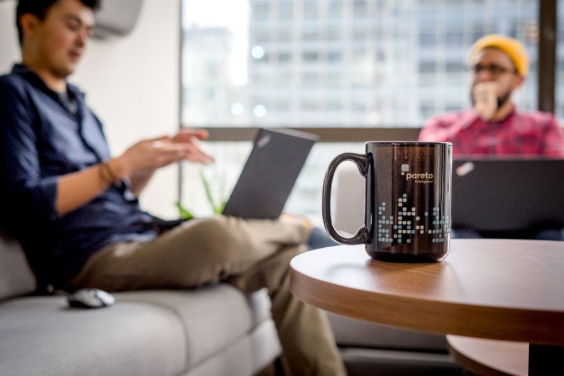 Pareto mug on a table with team members having a meeting in the background