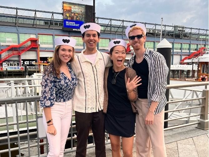  Four team members pose for group photo outside wearing Whatnot-branded sailor hats, near boat dock.