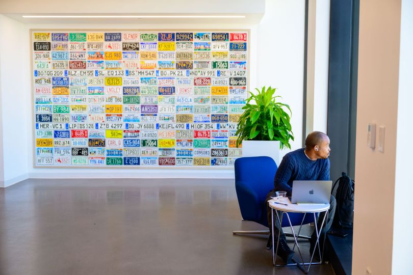 A CarGurus employee sits with a computer near a wall covered in license plates inside Boston’s new Lyrik Back Bay project at 1001 Boylston Street.