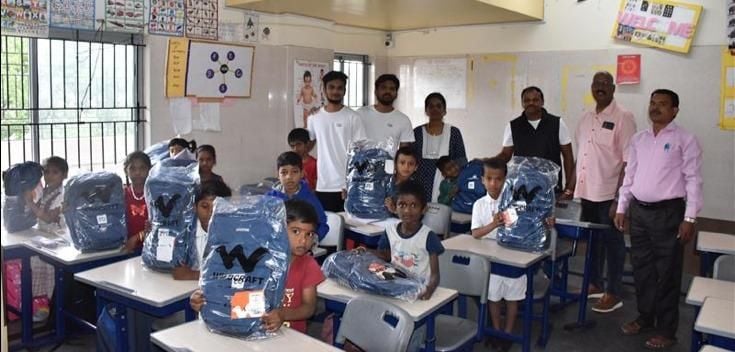 Q2 team members in a classroom with children showing their donated backpacks and educational supplies.