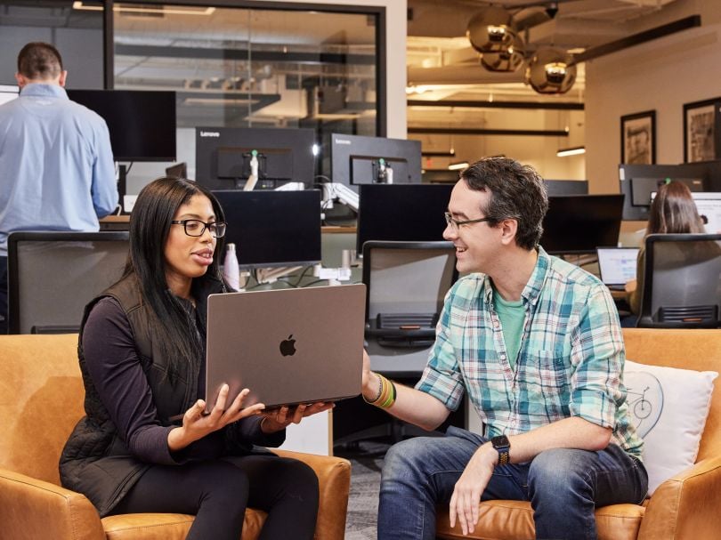 Rapid7 team members sitting on leather office chairs looking at a computer.