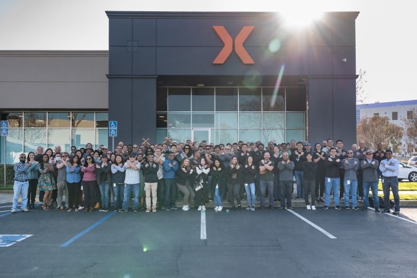 RefleXion employees stand in front of their building, which has a giant "X" on it