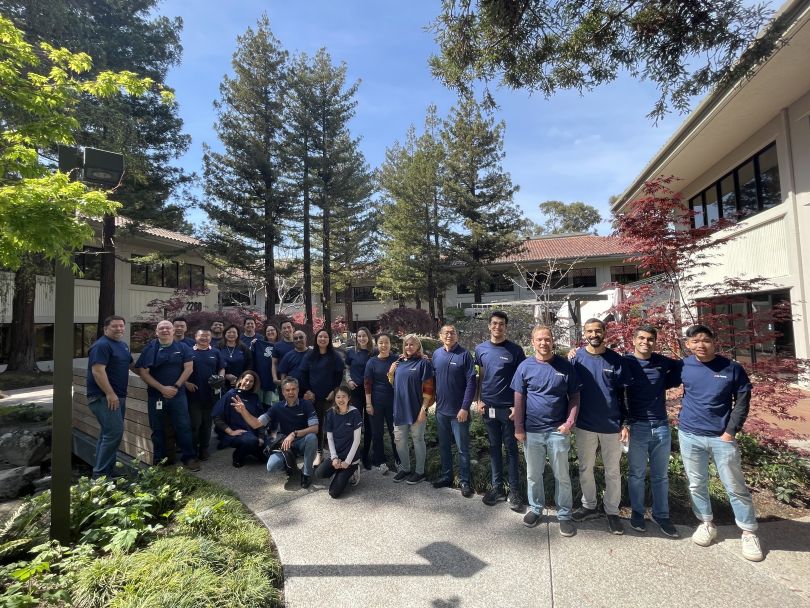 SambaNova employees stand together beneath trees and between buildings outside