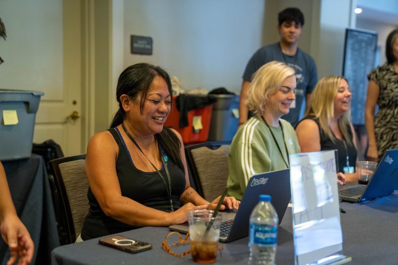 Rozlyn Ramirez takes notes on her laptop while chatting with coworkers during a company event