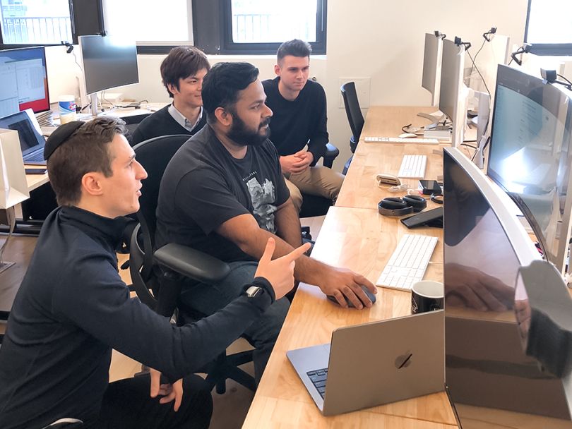 SIMON coworkers at a workspace have a team huddle looking at a computer monitor