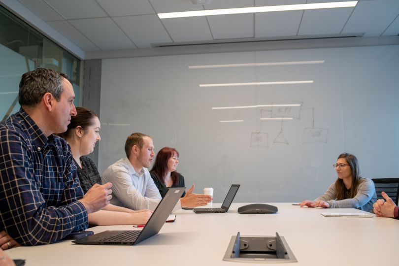 Photo of Takeda team members meeting around a conference room table with whiteboard in the background.